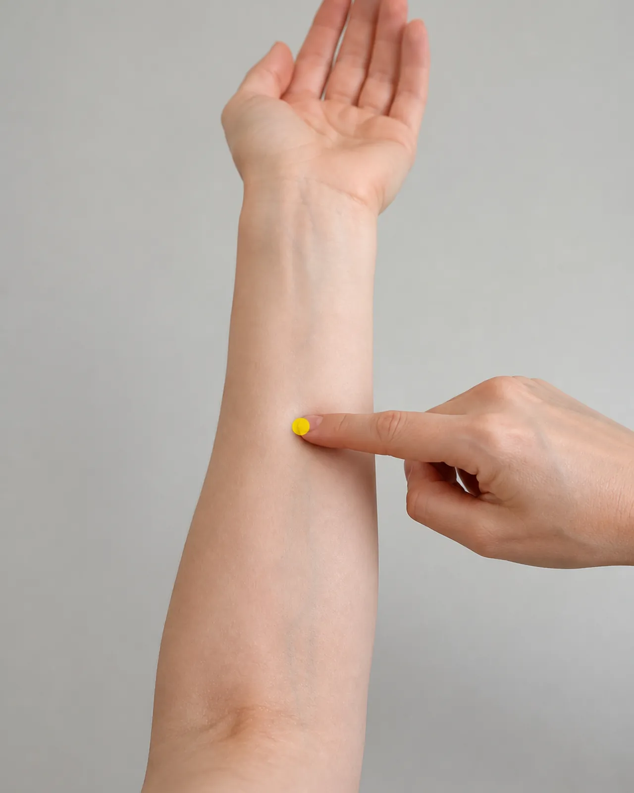 Index finger pointing to a yellow teaching mark at Chi Wei on the inner forearm midpoint between wrist and elbow crease