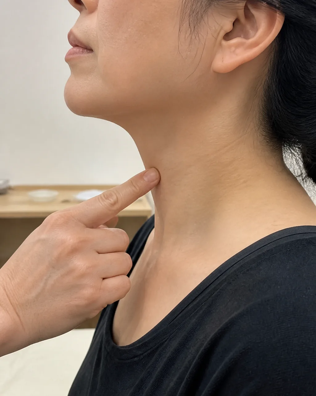 Finger locating Lian Quan CV23 above the hyoid bone on the neck