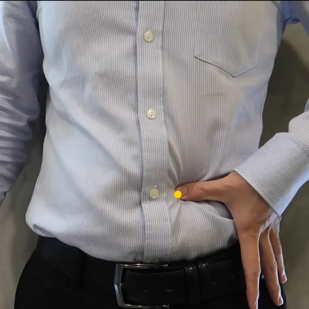 Three fingers measuring two cun lateral to the navel to locate Tian Shu ST25 on the abdomen, marked with a yellow dot