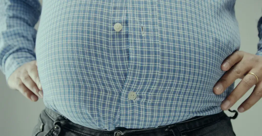 Close-up of a man's midsection in a tight checkered shirt showing abdominal obesity
