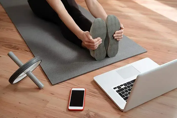 Person in a seated forward fold on a yoga mat following a laptop workout at home