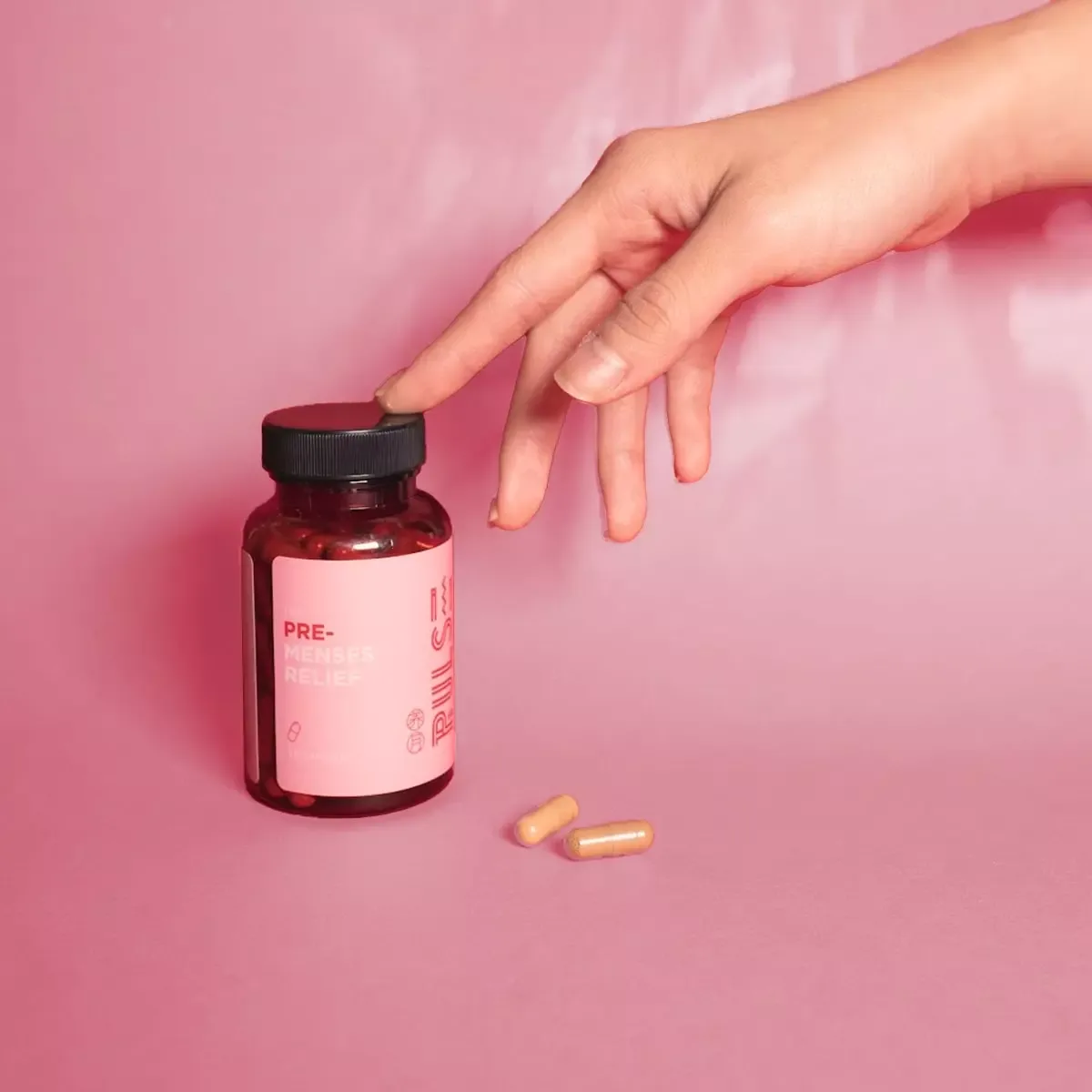 Hand opening a bottle of PULSE Pre-Menses Relief capsules