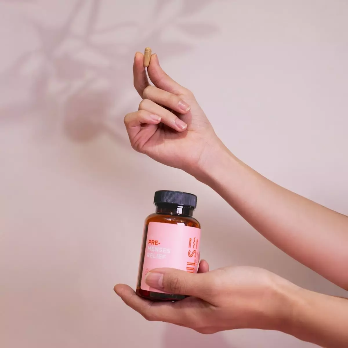 Hands holding PULSE Pre-Menses Relief bottle and one herbal capsule
