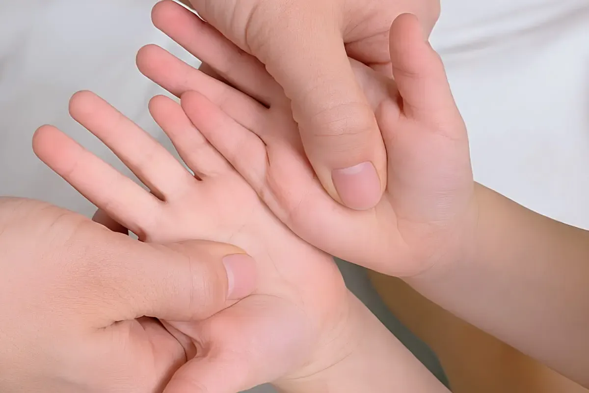 Adult thumbs gently pressing a child's palms during paediatric Tuina